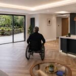 A man in a wheelchair in a modern adapted home with a view out to a well landscaped accessible garden.