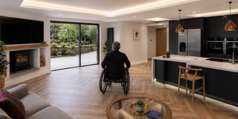 A man in a wheelchair in a modern adapted home with a view out to a well landscaped accessible garden.